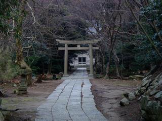 山の麓にある木々に囲まれた石の鳥居とその奥に建つ御島石部神社の写真