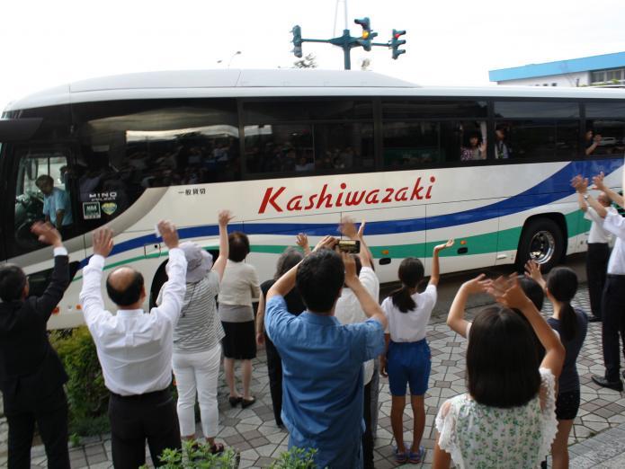 写真：ホストファミリーの皆さんが成田空港に向かうバスに手を振り、見送っています