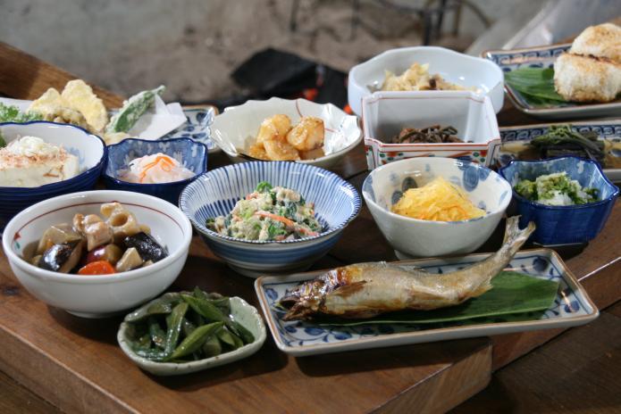囲炉裏端に山菜や焼き魚など、いろいろな料理が並んでいる写真