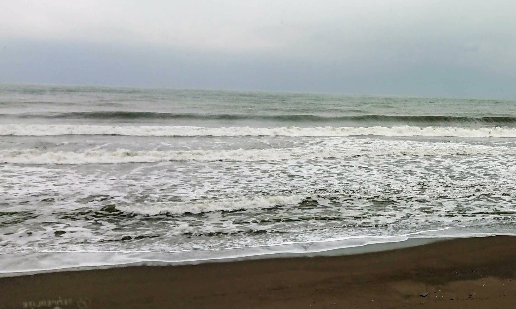 写真：沖のほうから高い波が発生し、危険な海の様子。泡立った白い波が広がっています。空には灰色の雲が広がっています