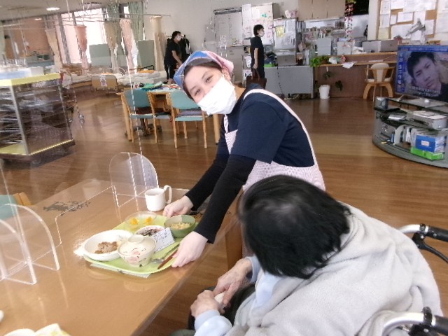 写真：利用者の食事を運ぶ女性が写っています。
