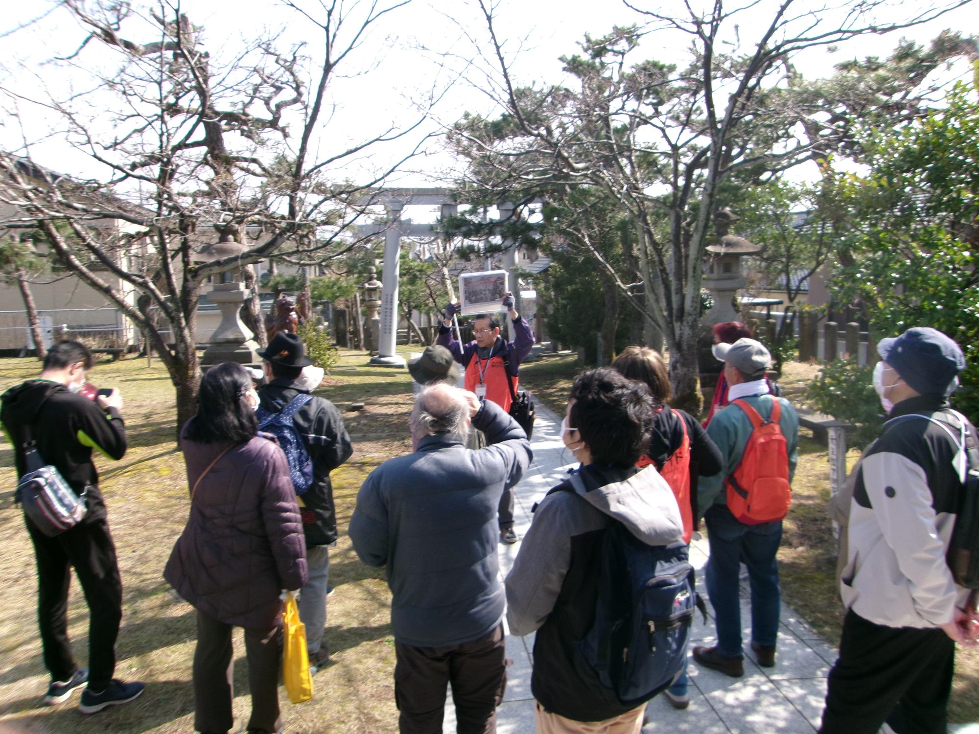 写真：石井神社で解説するボランティアガイド。ガイドの後ろに石造りの鳥居が見えます