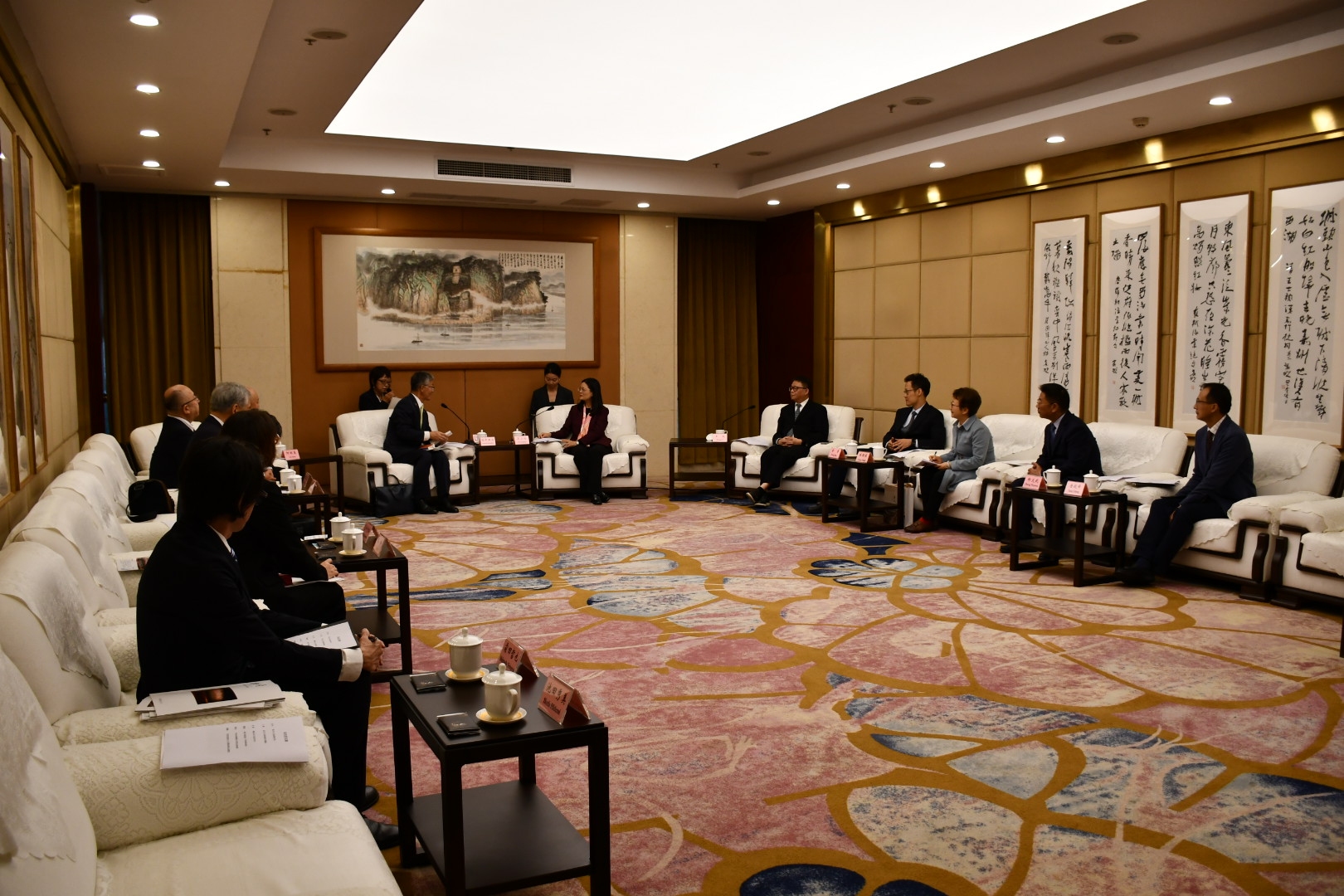 写真：首脳会談全体の様子。広い応接室にコの字型に一人掛けのソファが並べられ、左側に柏崎市側、右側に楽山市側の関係者が座っています。