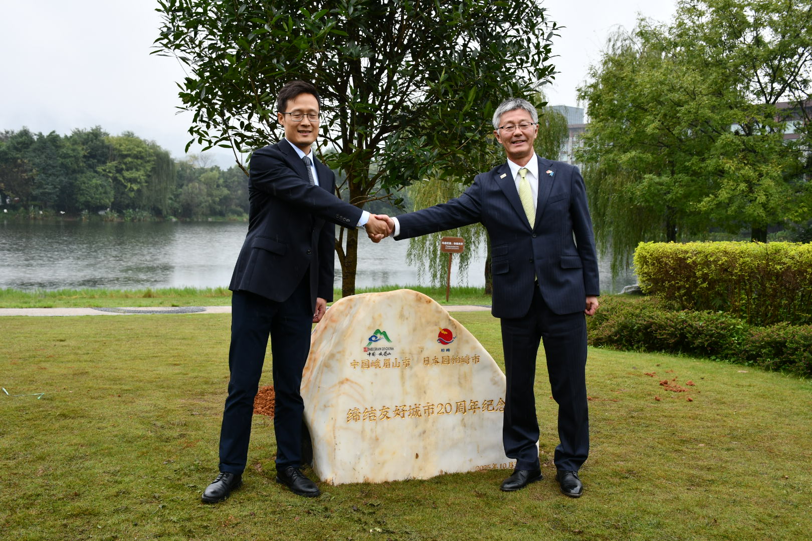写真：庭園で友好都市20周年を記念した石碑の前で櫻井市長と峨眉山市長がにこやかに握手をしている様子