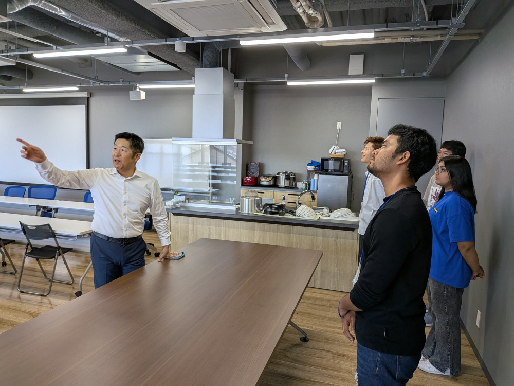 写真：阿部建設の男性社員が学生たちに社屋の特徴を指さしながら説明しています