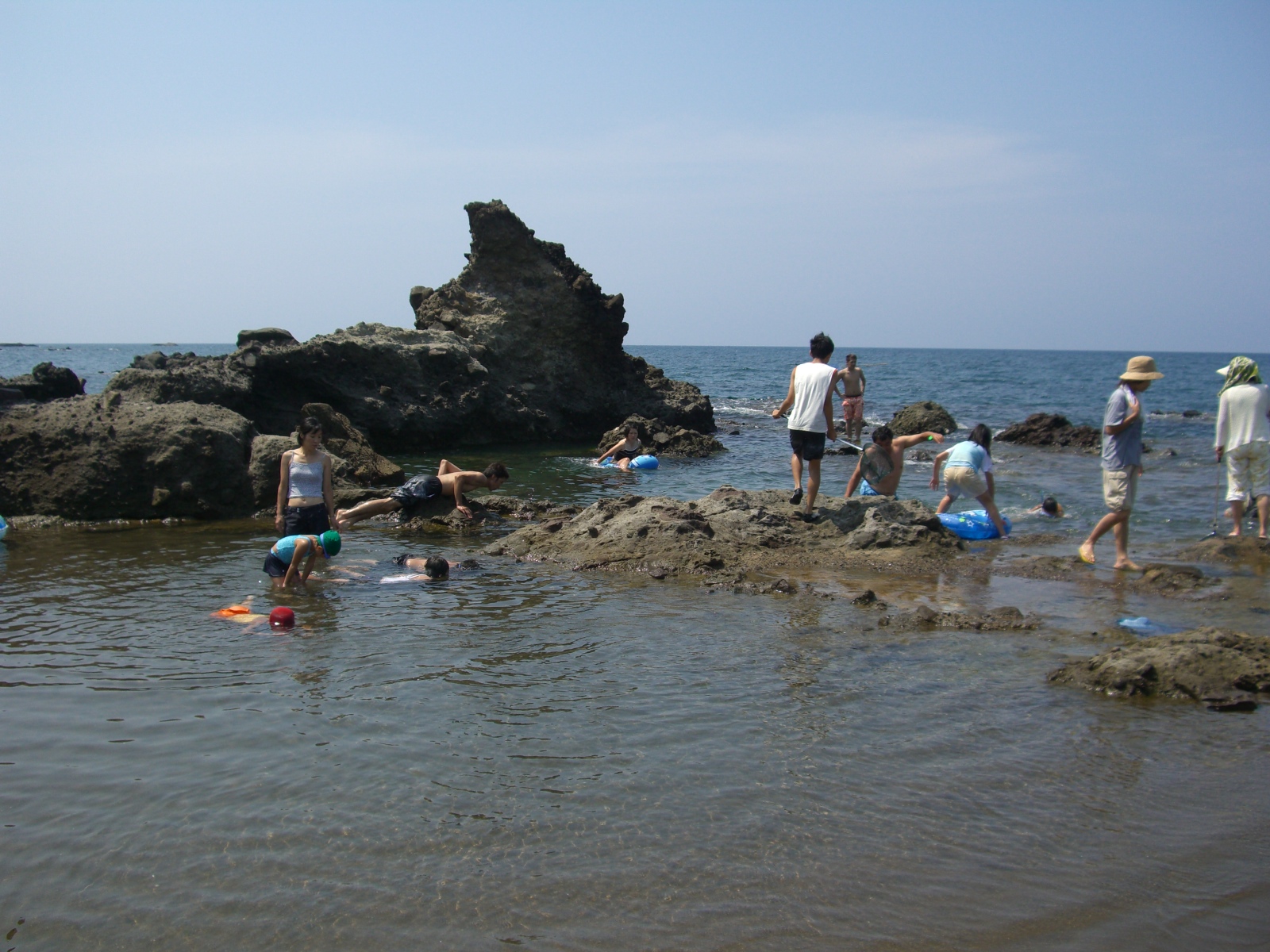 薬師堂海水浴場の中央に岩場があり岩の上に立って遠くを眺めている人や海水で遊ぶ子どもたちの写真