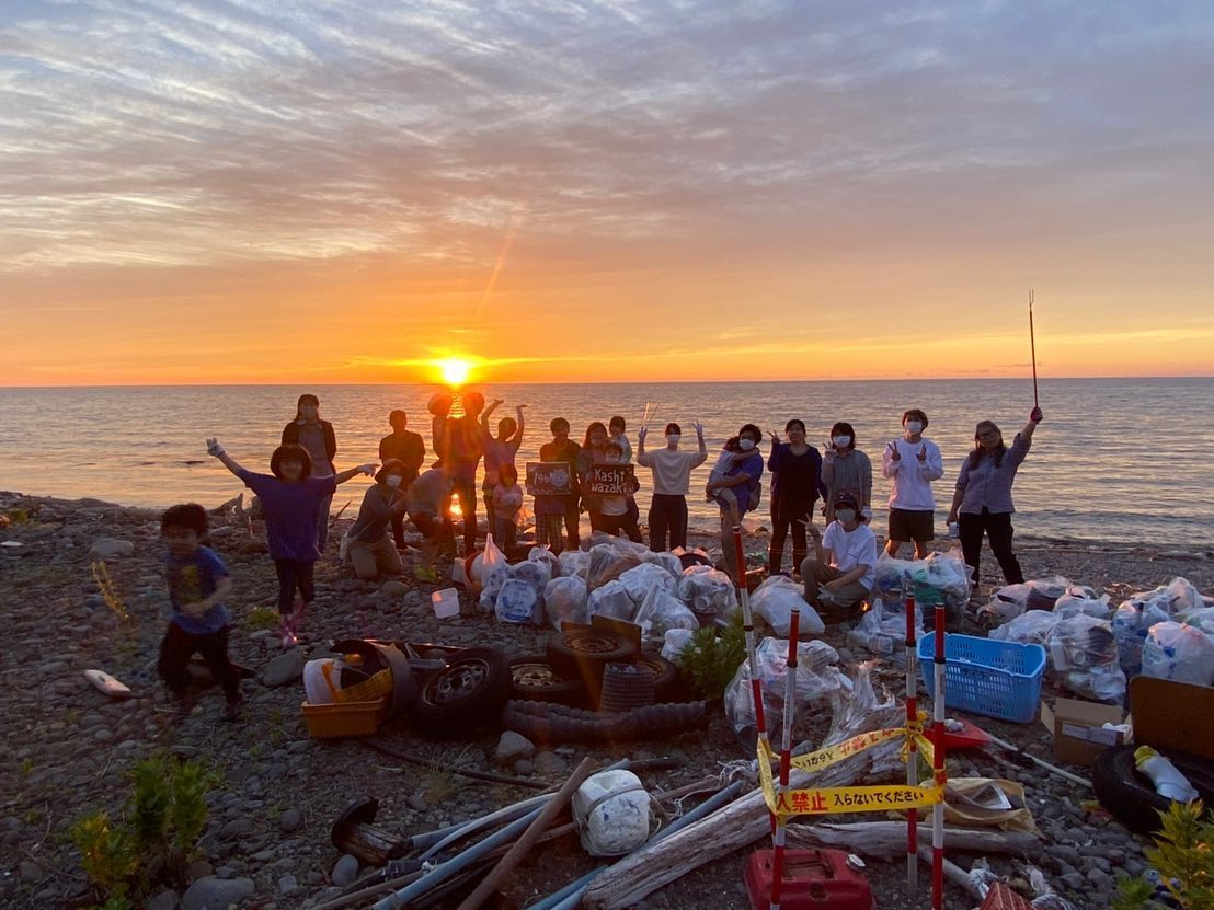 日本海に沈む夕日と海岸清掃に参加した皆さんの写真