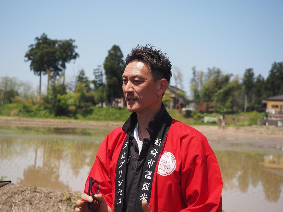 写真：田植えを終えたばかりのほ場の前でコメントする重野貴明さん。