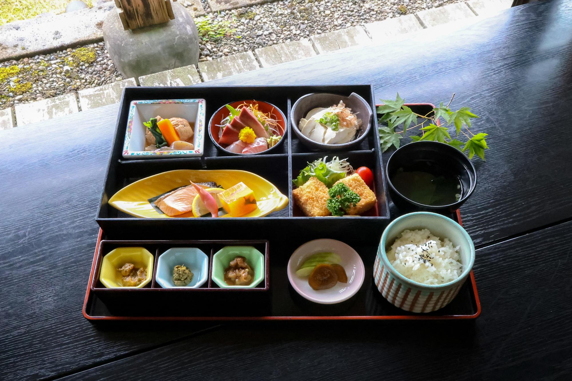 写真：ご飯と味噌汁、刺身や焼魚、揚げ物、煮物など多数の小鉢が並んでいます