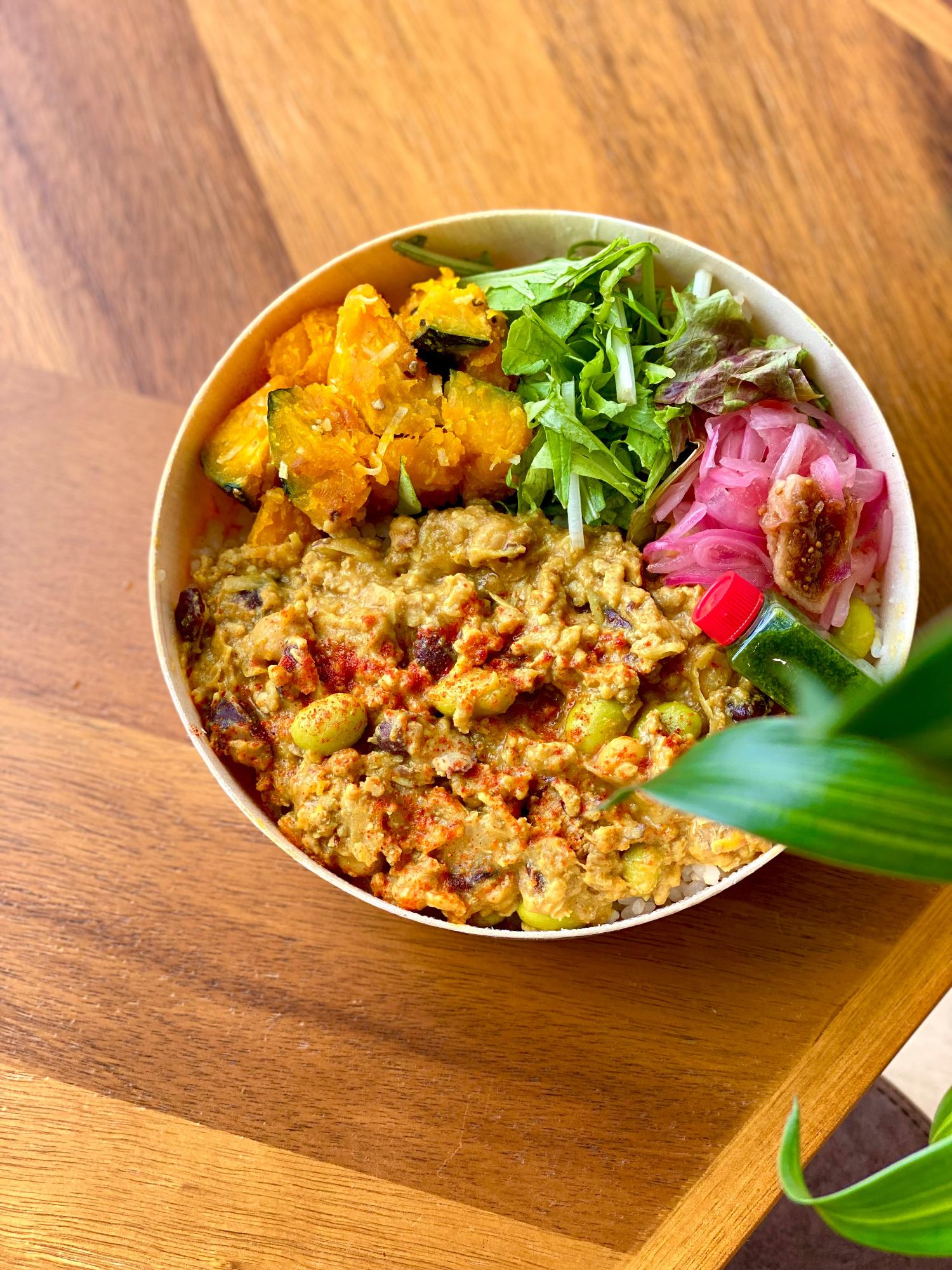 写真：枝豆の入ったキーマカレーに、かぼちゃサラダや水菜などを添えた彩り鮮やかなお弁当です