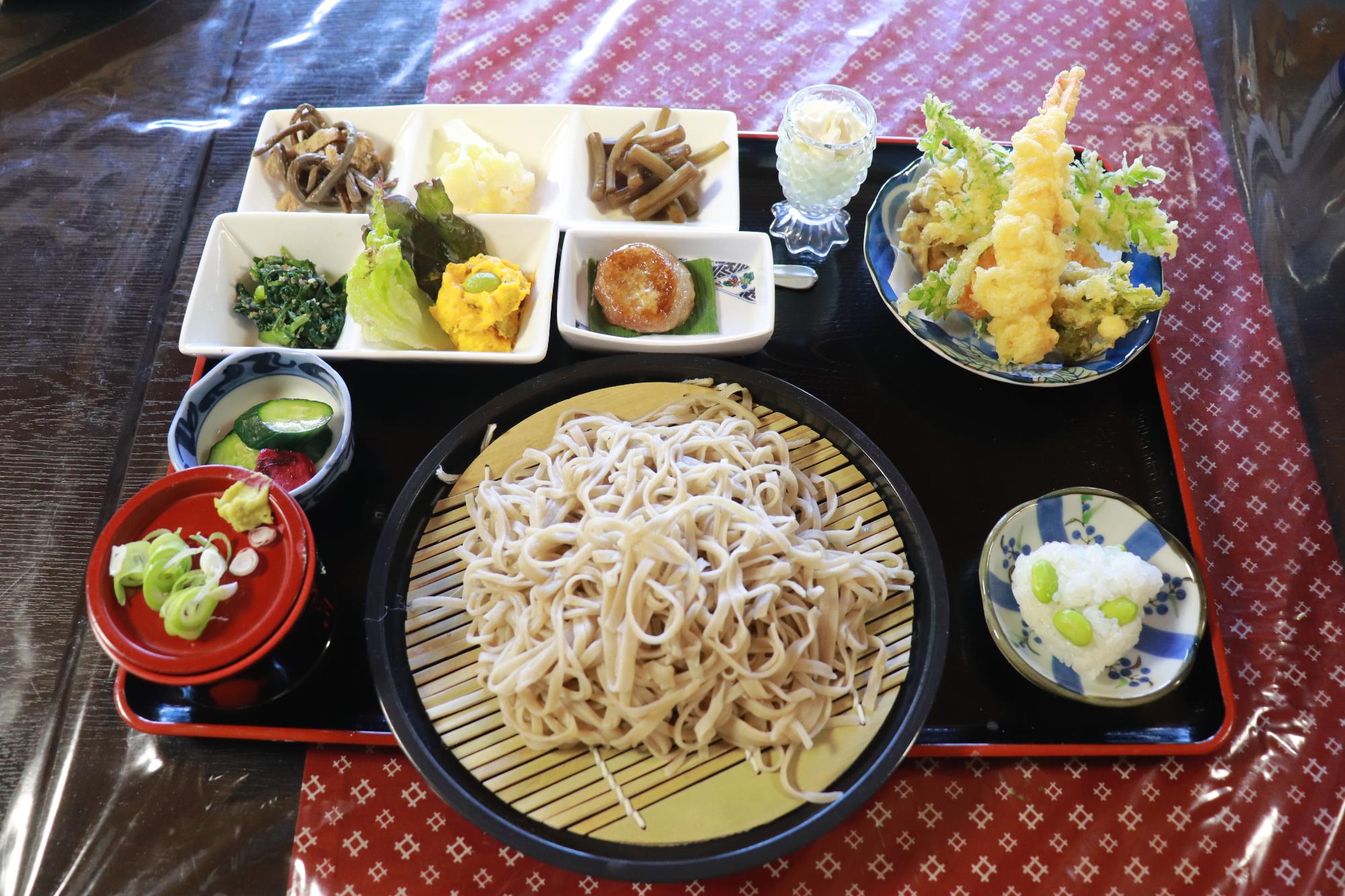 写真：手打ちそばに、季節の山菜やエビの天ぷら、野菜をふんだんに使った煮物や和え物などの小鉢がセットになっています
