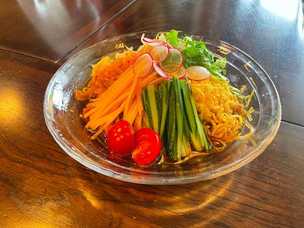 高柳じょんのび村の萬歳楽の中のお食事処やまどりで提供される夏野菜たっぷりじょんのび冷やし中華です。面の上にきゅうり、ニンジン、トマトなどの夏野菜がたっぷりのっています。