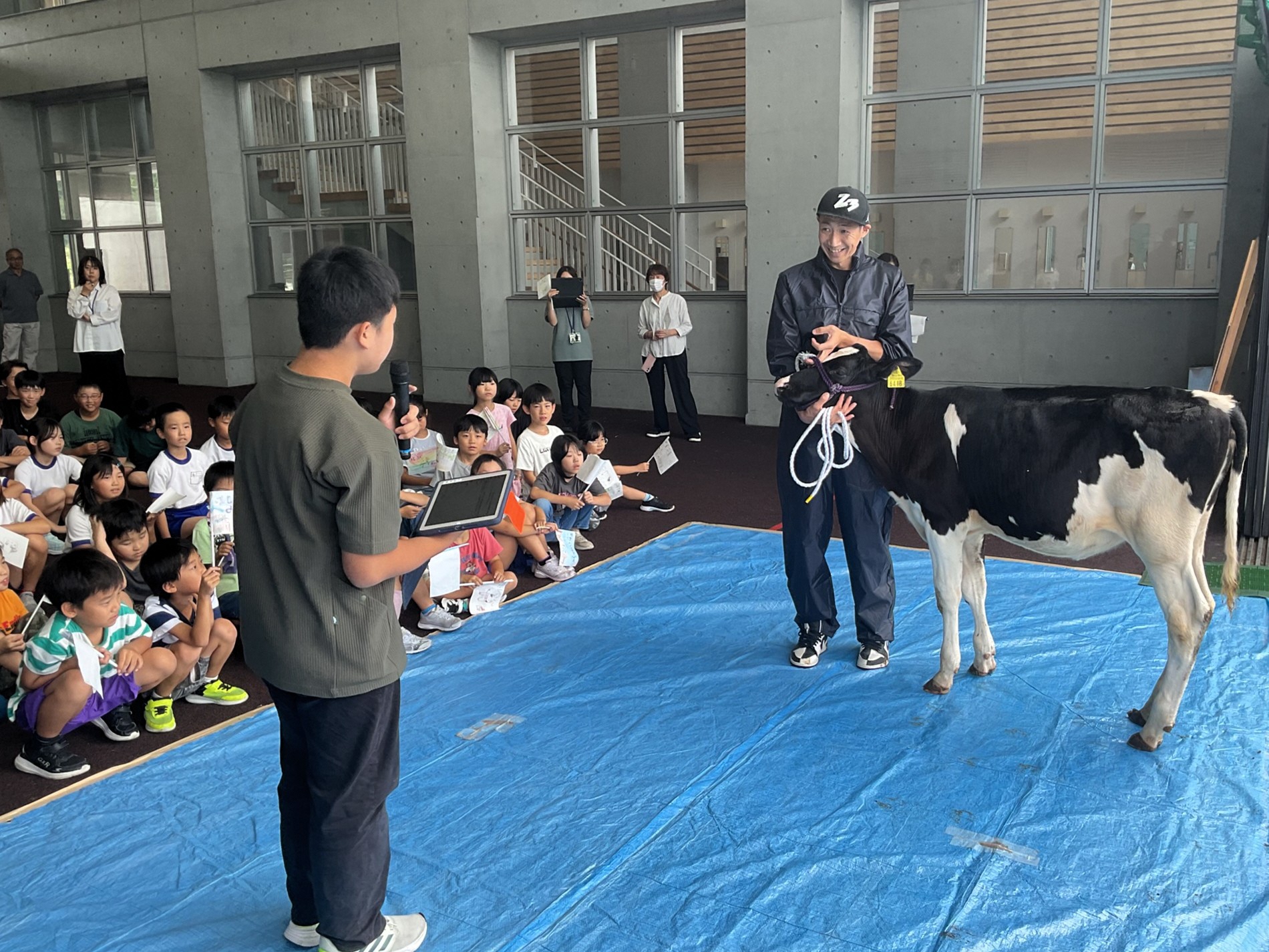 写真：6年生の男の子が江部さんと牛の前に立ち、卒業証を読んでいます。