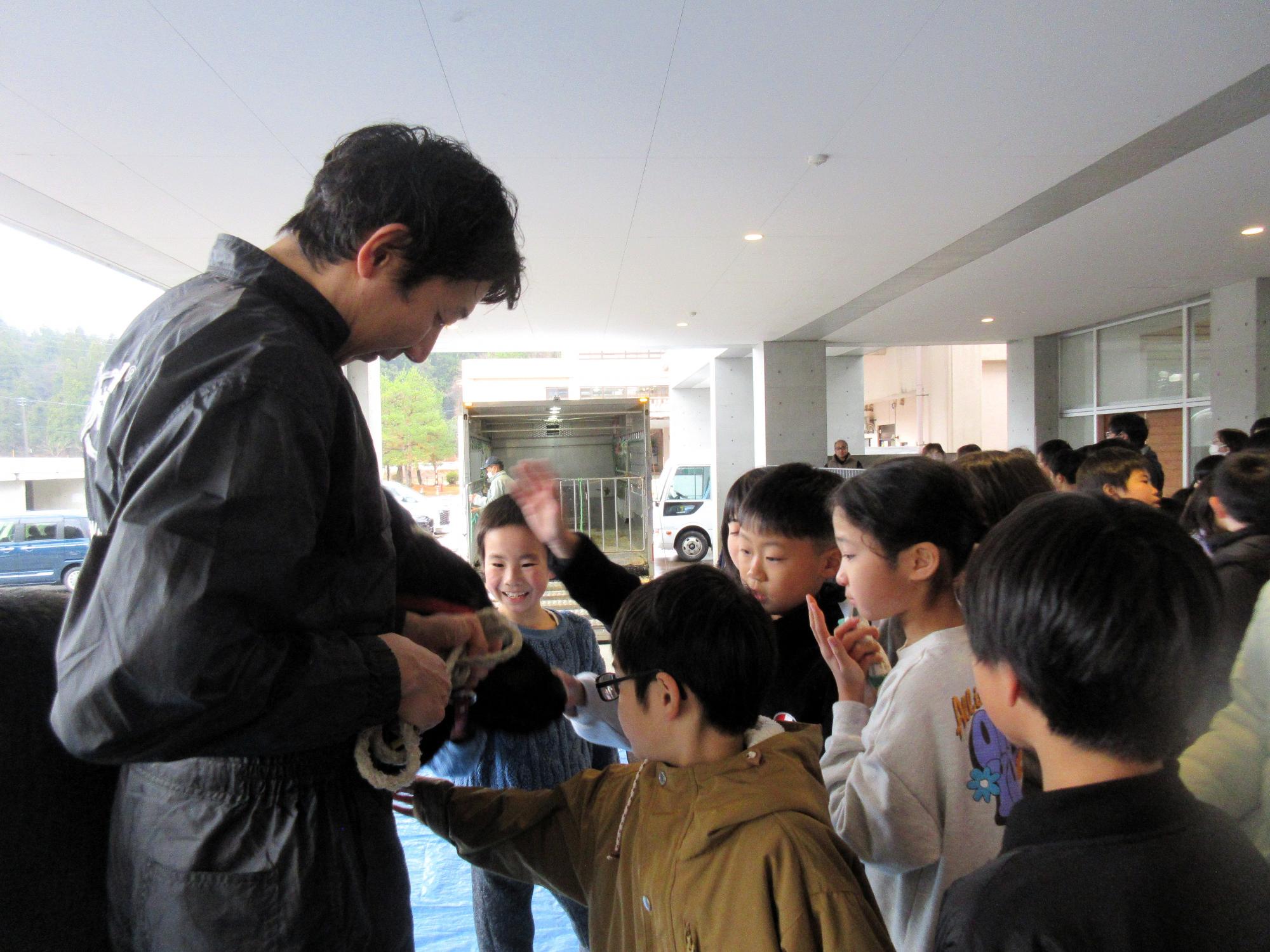 写真：江部さんの脇にいる牛を触る小学生の子どもたち