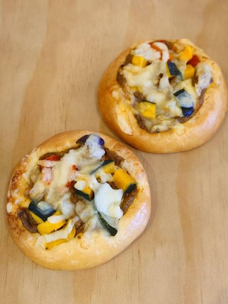 ぱん工房満天のかぼちゃと夏野菜のチーズカレーの写真です。パン生地にかぼちゃとズッキーニやパプリカなどの夏野菜の入ったカレーに上からチーズがのっています。