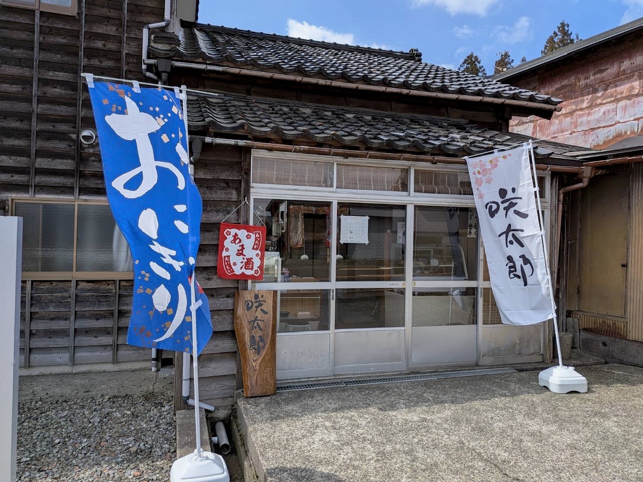 写真：かのう咲太郎の外観です。木に咲太郎と書かれた看板が店の前にあり、おにぎりと咲太郎と書かれたのぼり旗が並んでいます。