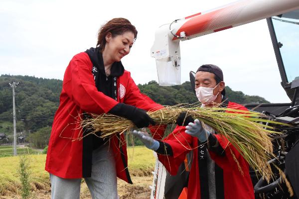 写真：刈り取った稲を脱穀するため、越乃リュウさんが徳永さんへ稲を受け渡しています