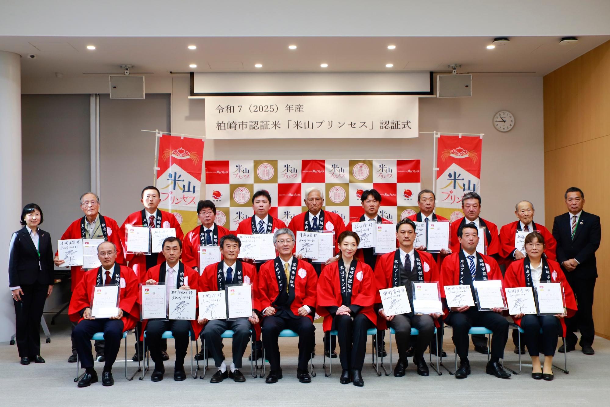 写真：認証状とメッセージ色紙を持った認証者15名と櫻井市長、アンバサダーの越乃さん、柏崎地域振興局農業振興部副部長の本間さん、えちご中越農業協同組合かしわざき営農センター長の佐藤さんがカメラに収まりました。