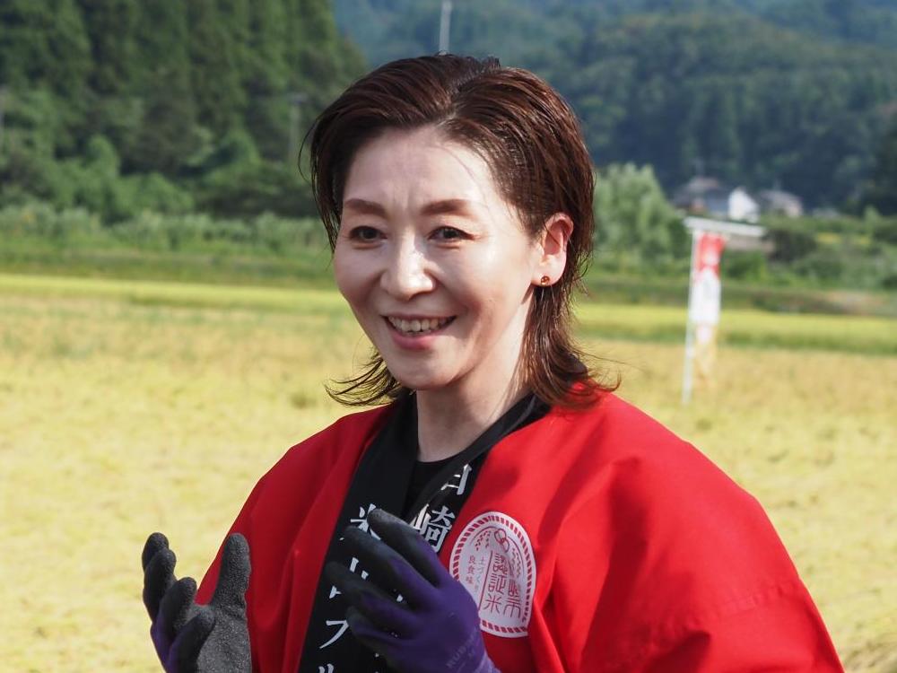 写真：両手に稲刈り用の手袋をしたままインタビューに答えるアンバサダーの越乃リュウさん