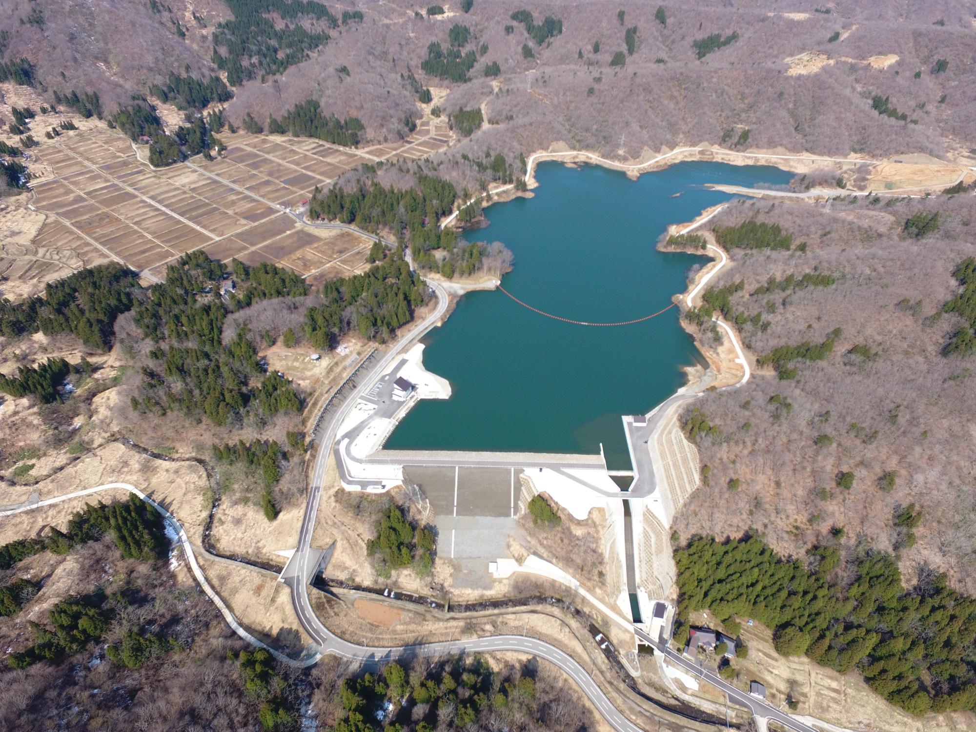 写真：市野新田ダムの全景。青く美しいダム湖や、表面を石で覆った構造の堤体などが写っています