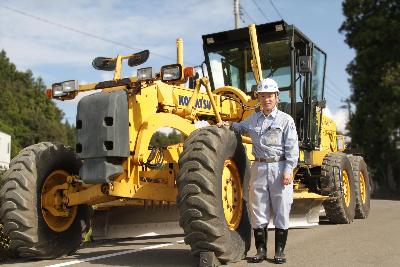 写真：大きな工事車両のそばに立つ木戸さん