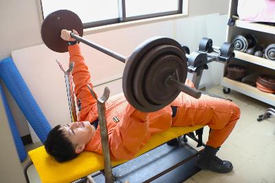 写真：消防署のトレーニング室でバーベルを持ち上げる山田さん