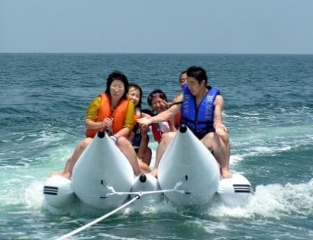 海の上を白いバナナボートに男女が乗って走っている写真