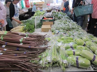 生産者が持ち込んだ新鮮な野菜と、買い求める人でにぎわう店内の様子の写真