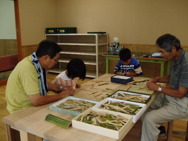 子どもたちが大人の指導で竹細工をしている写真