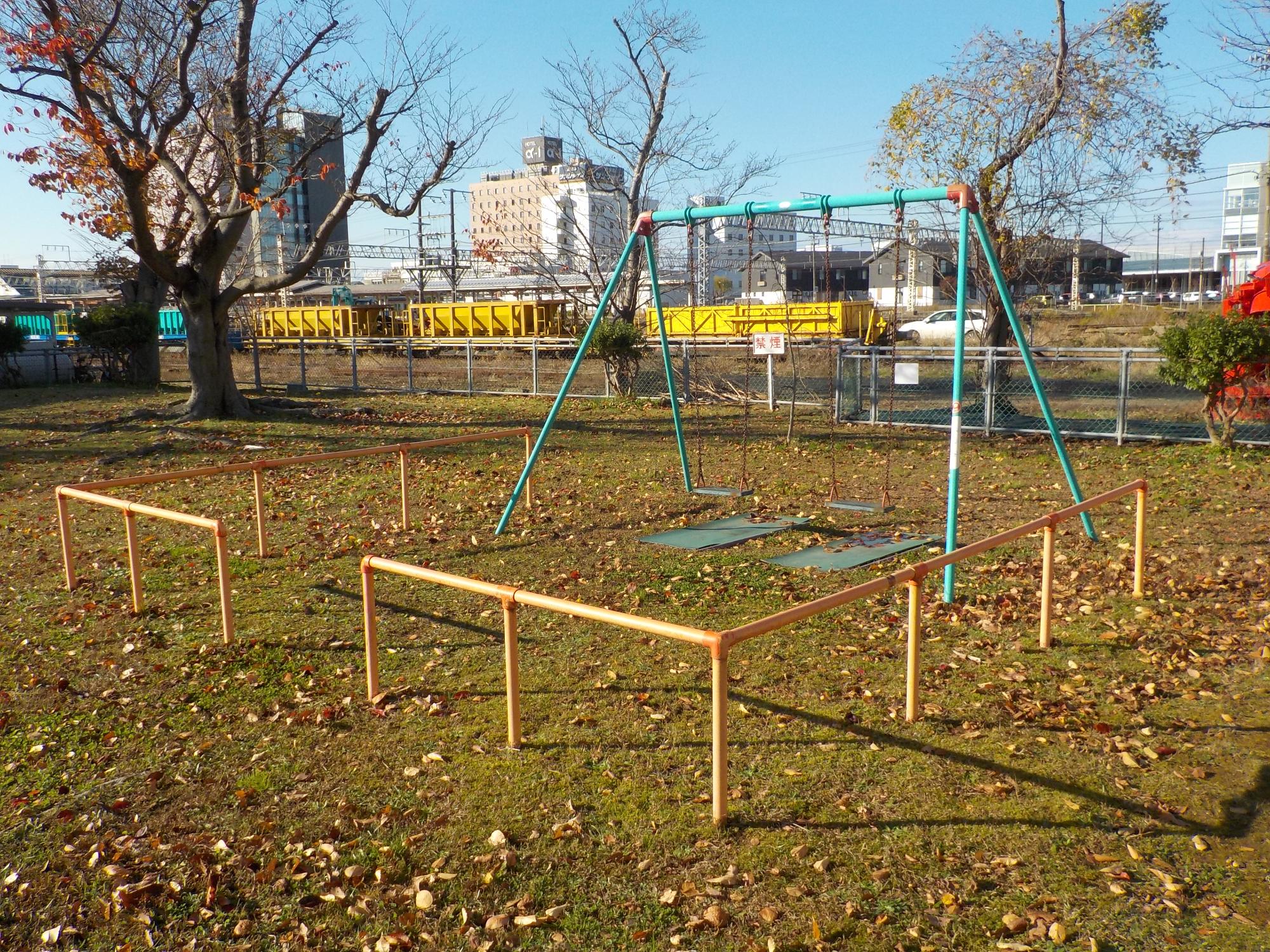 写真：2つのブランコがあります。奥に線路が走っています。