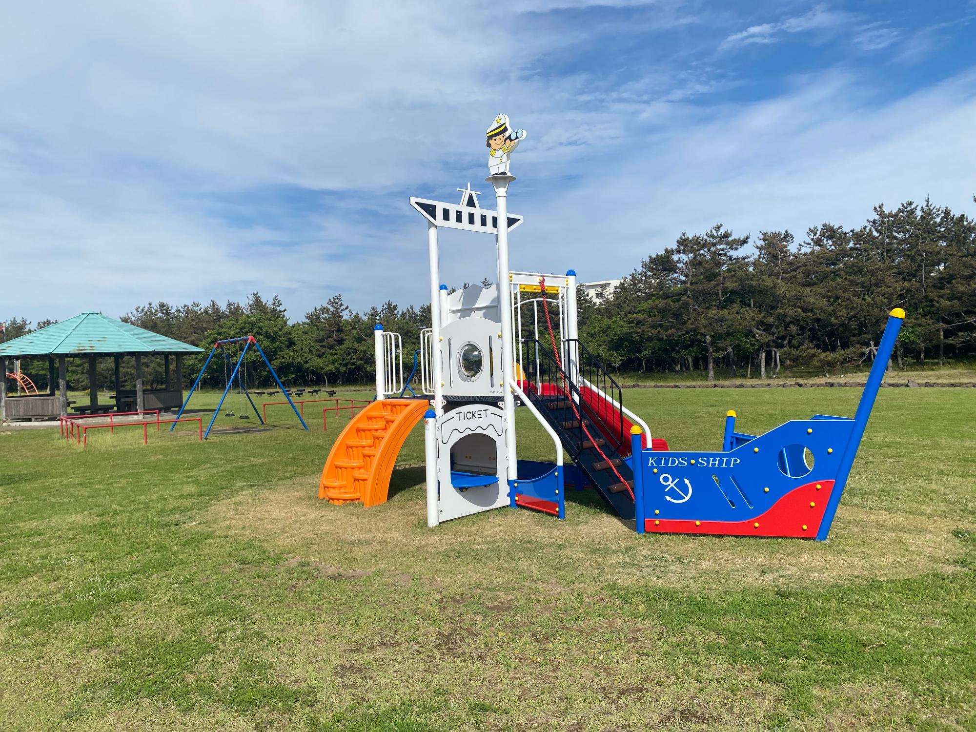 写真：手前に船を模した幼児用の複合遊具が、奥にはブランコが、さらにその奥には休憩用の東屋もあります。