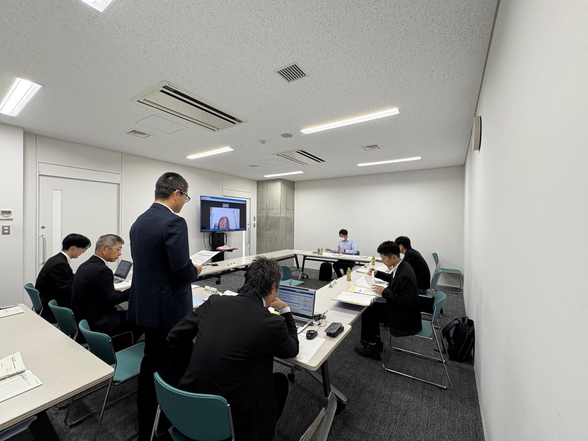 写真：第2回審議会の様子。市役所会議室で、委員が市職員からの報告を受けています。