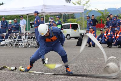 写真：一番員が片足でホースの一端を抑え、もう一端を手に保持しながら、巻き取ってあったホースを前方に展張している様子