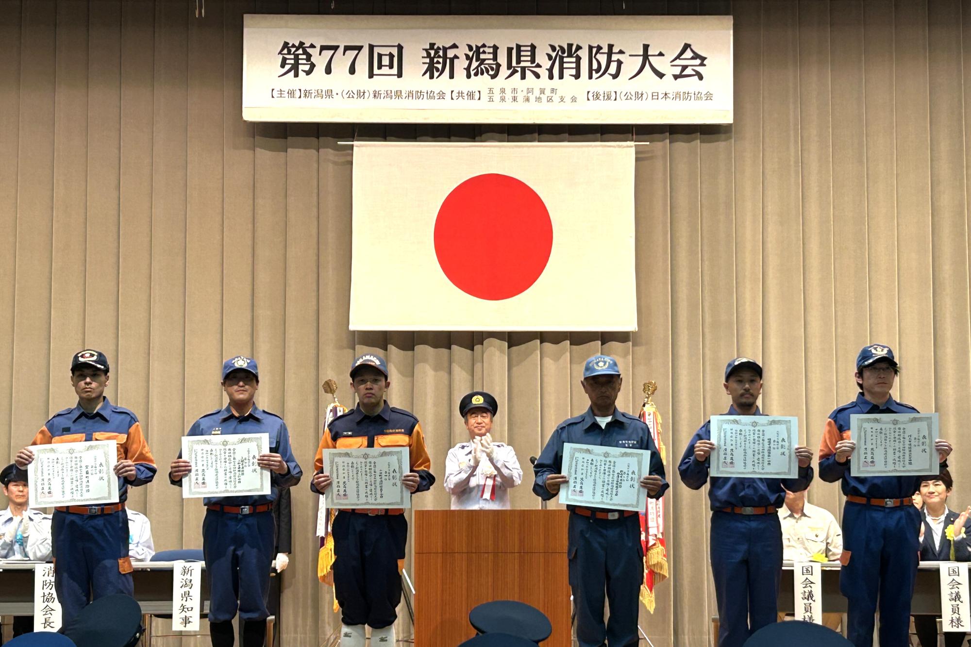 写真：入賞した分団が横一列に並び、観客席に受け取った賞状を見せている様子