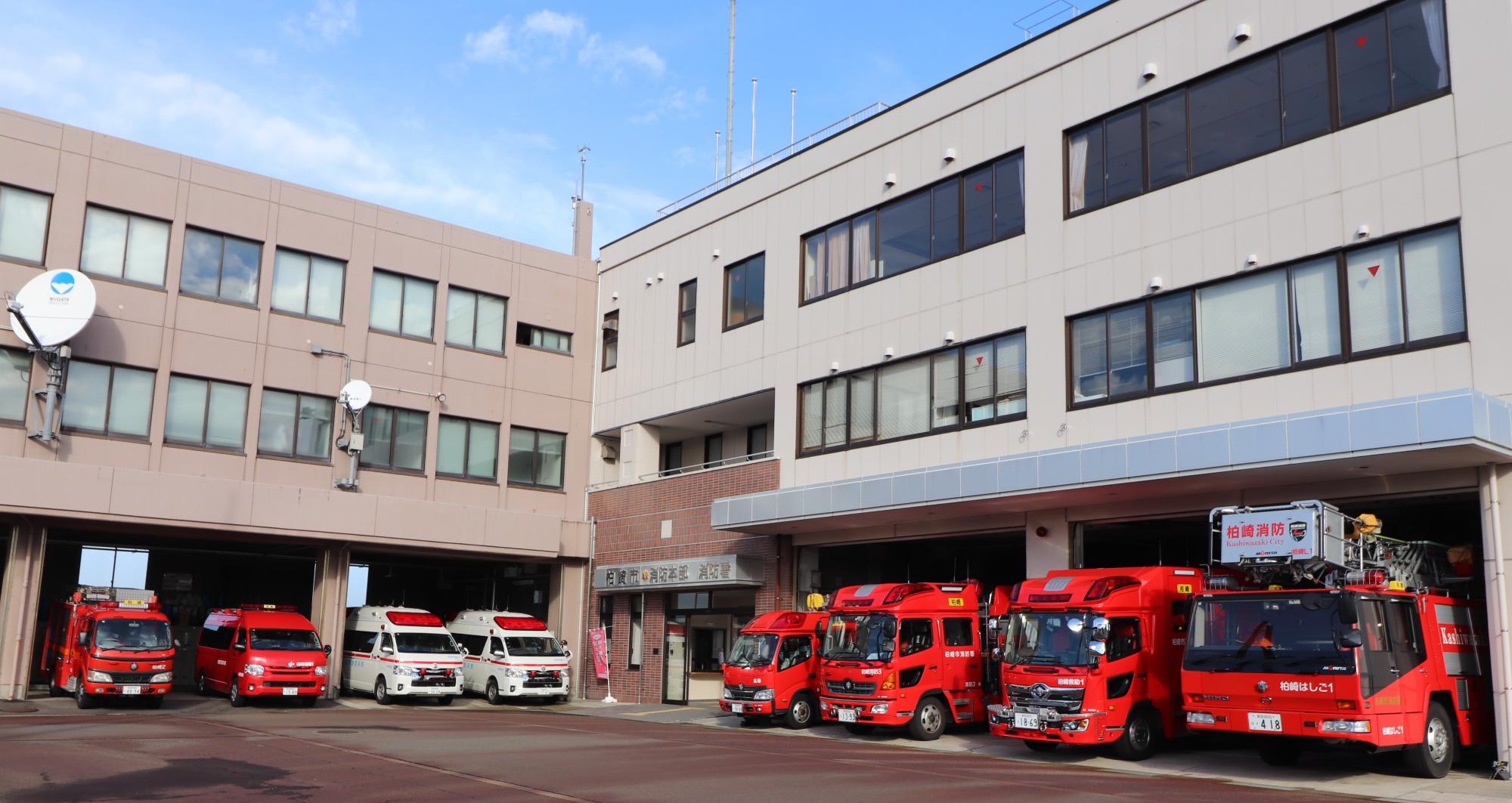 消防本部の前で消防車や救急車などの緊急車両が並んでいる写真