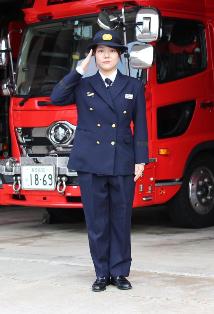 消防車両の前で紺色の制服を着た女性消防職員が立っている写真