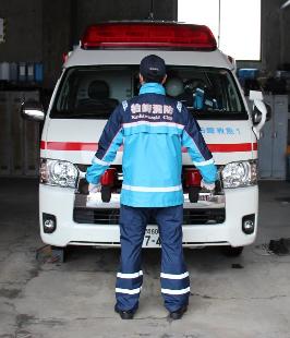 救急車の前で感染防止衣を着た男性救急隊員が後ろ向きで立っている写真