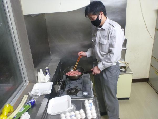 若手の職員が夕食の準備で、ひき肉を炒めている写真