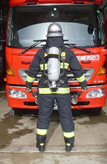 消防車の前に防火服と空気呼吸器を着装した消防隊員が後ろ向きで立っている写真