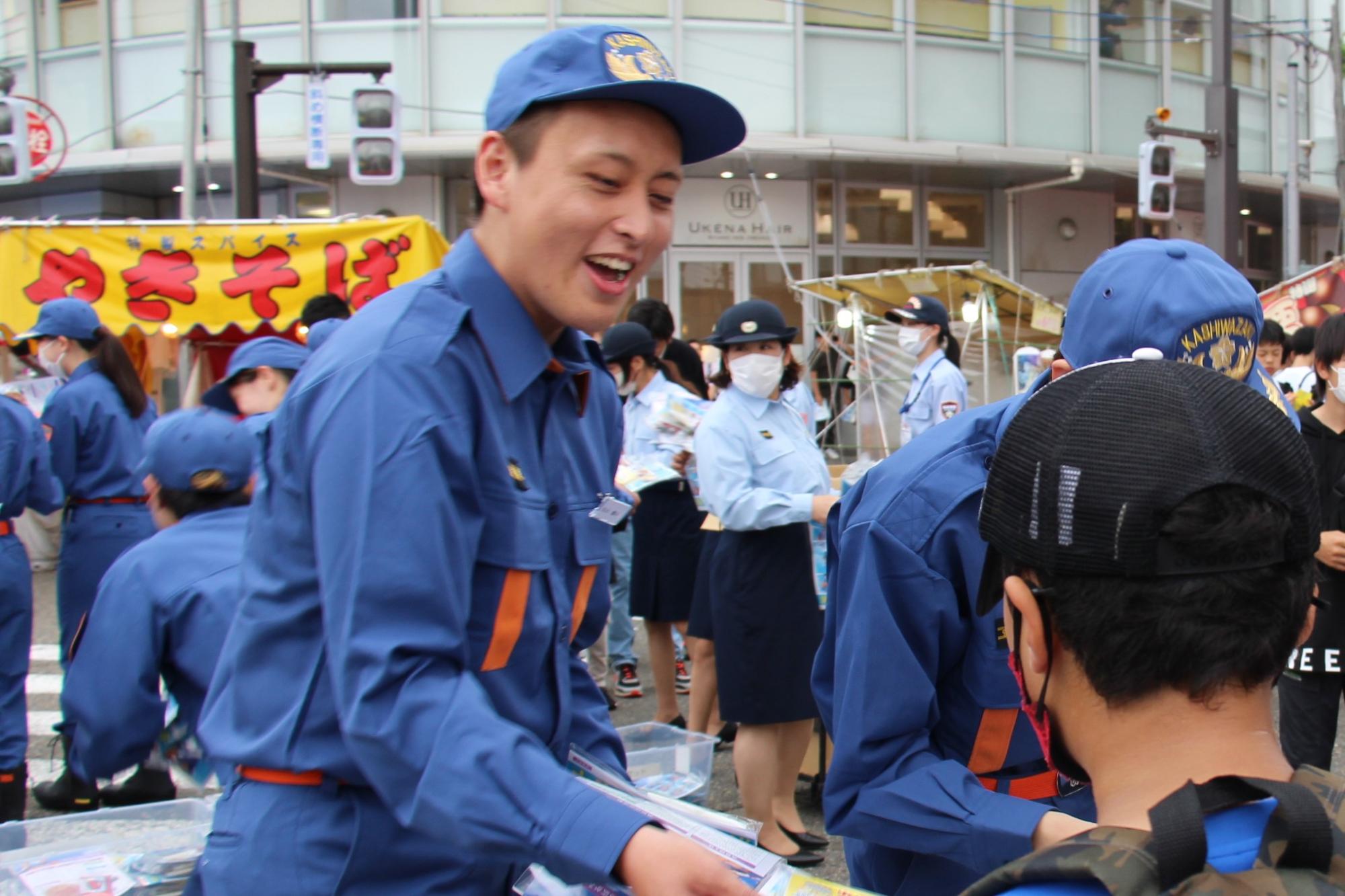 写真：学生消防隊員が笑顔でパンフレットを手渡しています
