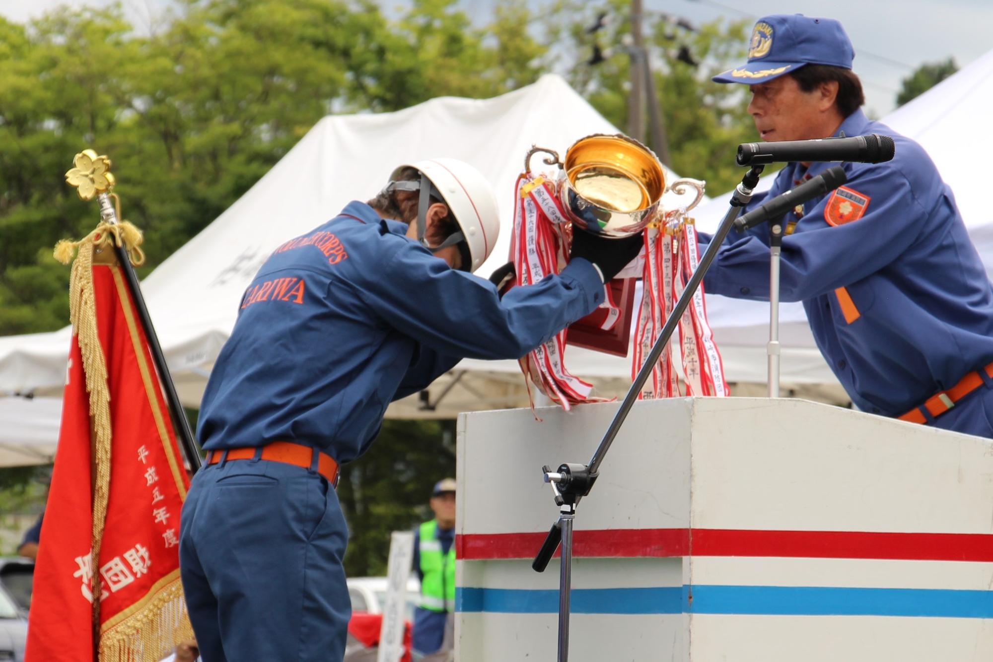 写真：地区支会長から優勝トロフィーを授与される刈羽村消防団員