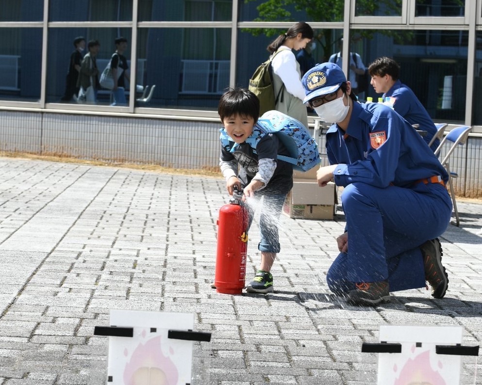 写真：水消火器の水を目標物に向かって噴射する子どもと隣で付き添う学生消防隊員