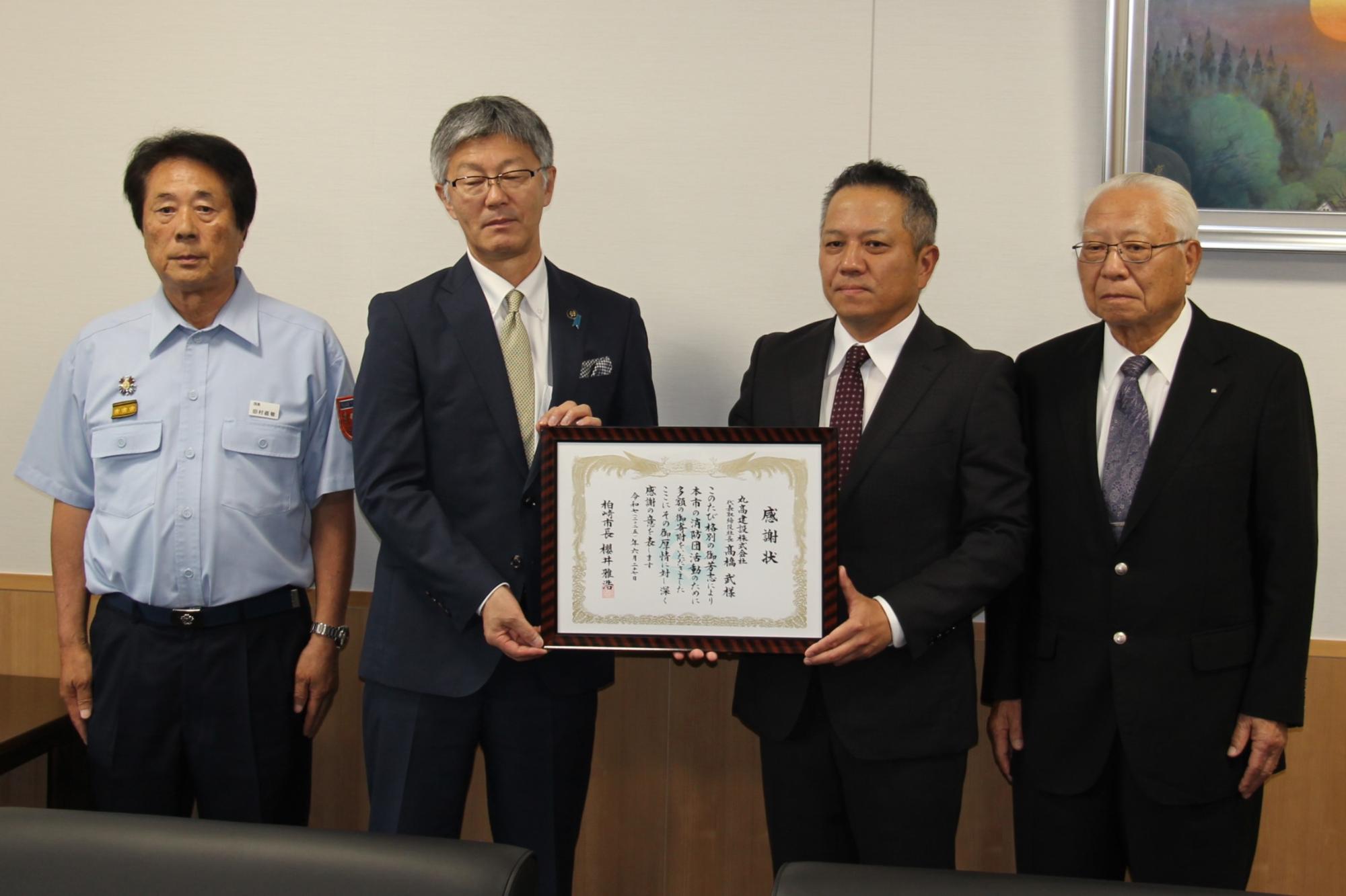 写真：左から順に、柏崎市消防団長、市長、丸高建設株式会社代表取締役社長、代表取締役会長が並んでいます。市長が丸高建設株式会社代表取締役社長に感謝状を贈呈しています。