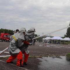 写真：ヘルメットに防火服を身に着け、二人で消火用ホースを操作する消防団員