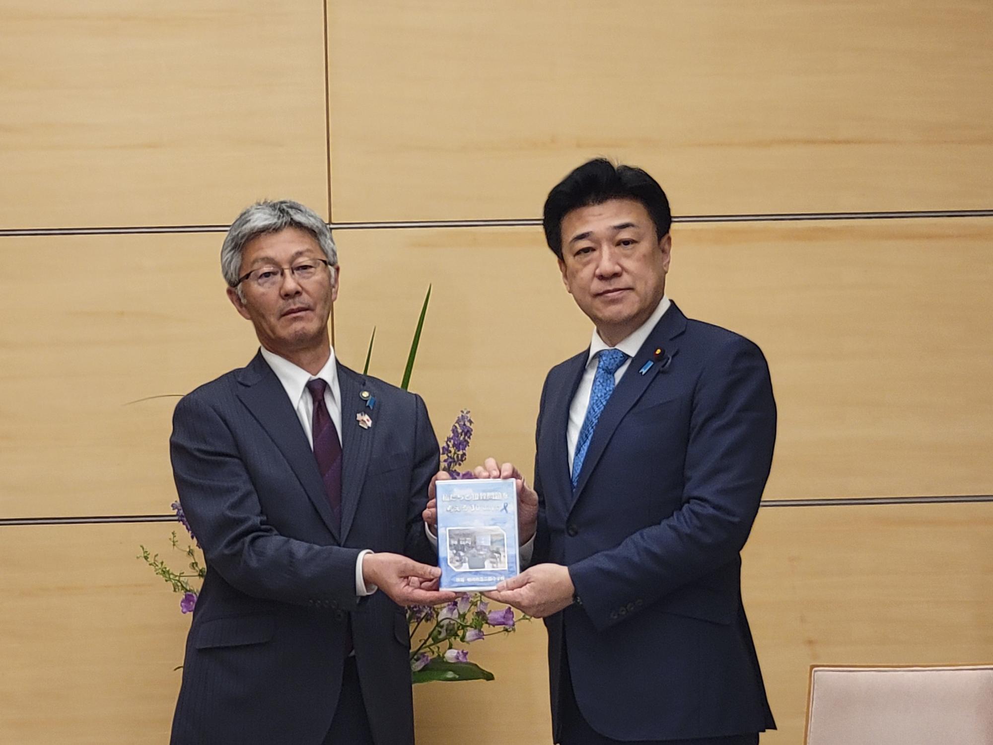 写真：木原内閣官房長官兼拉致問題担当大臣に柏崎市立二田小学校6年生が作成した作成した取組成果品を手交する櫻井市長。
