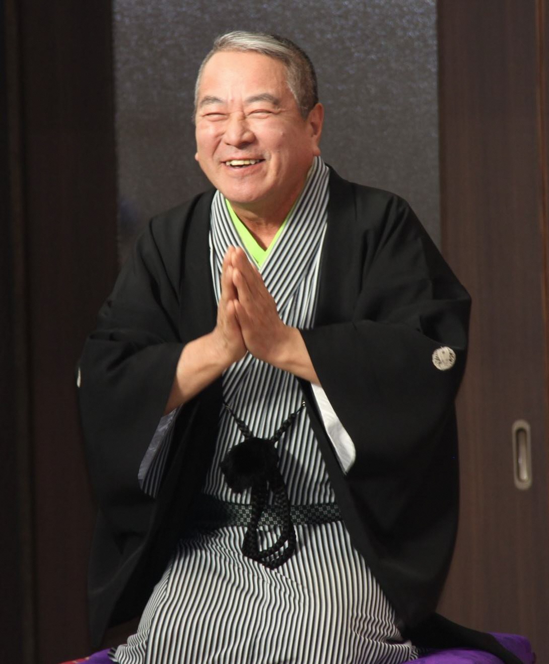 写真：黒白の縦じまの着物に、黒い羽織をはおり、笑顔で落語を披露する水都家艶笑さん