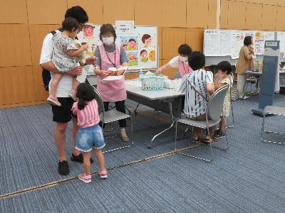 写真：親子でむし歯予防‼ 歯科衛生士がお子さんを抱っこしたお父さんに、むし歯の予防について説明しています。