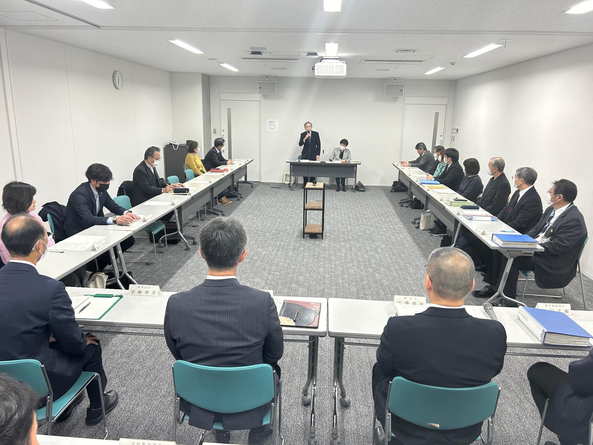 写真：会議の様子。手前に桜井市長と近藤教育長が座り、向かいに報告者がいます。両側には審議会の委員らが座っています。