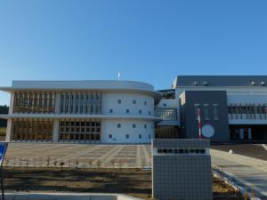 左側に丸みを帯びた2階建ての校舎と右側の角のある校舎のある近代的な第五中学校の校舎を正門から撮影した写真