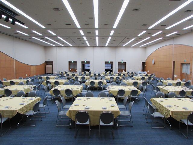 青いカーペットの敷かれたホールに、正方形のテーブルがいくつも並んでいる写真